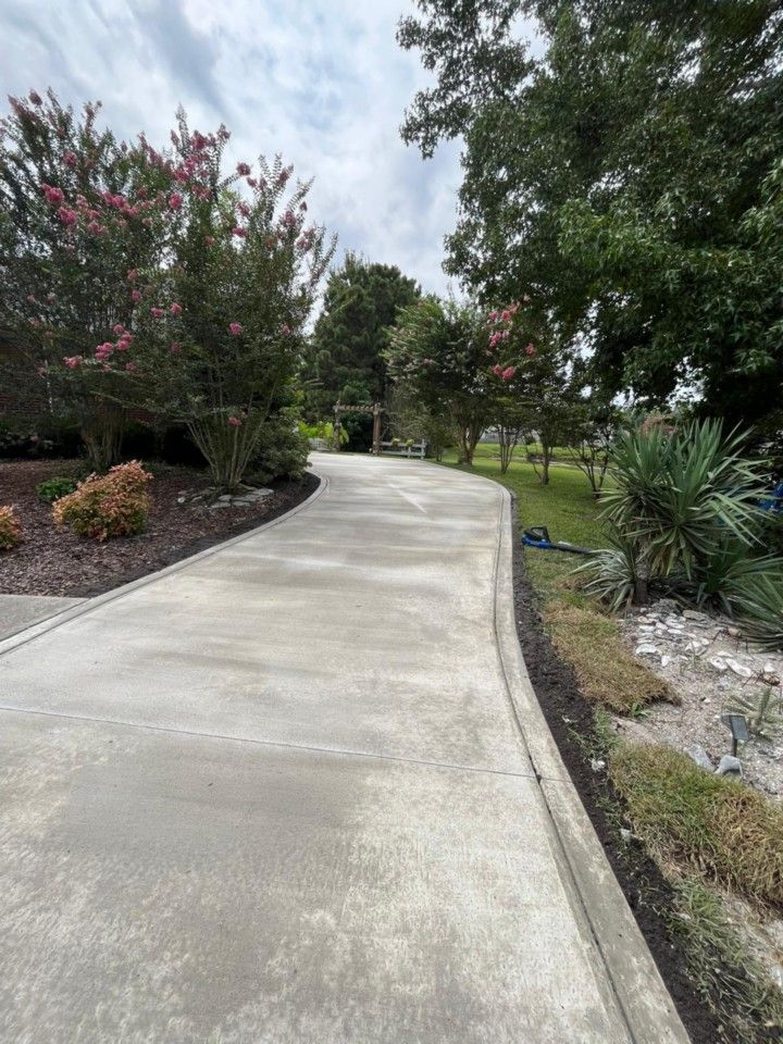 A concrete driveway leading to a house surrounded by trees and bushes.
