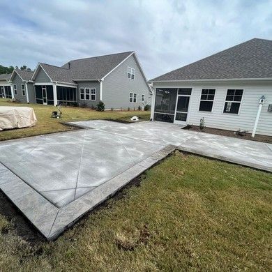 A concrete patio in front of a house with a screened in porch.