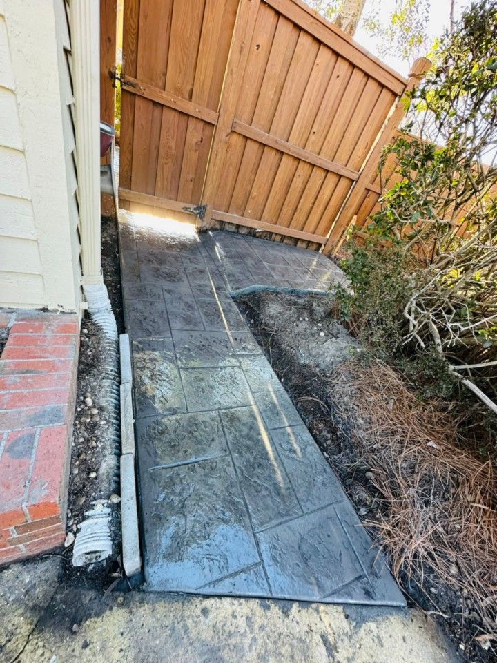 A concrete walkway is being built next to a wooden fence.