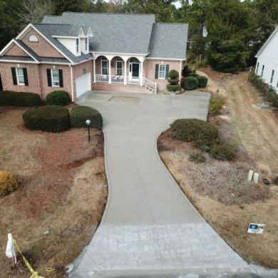 An aerial view of a brick house with a concrete driveway leading to it.