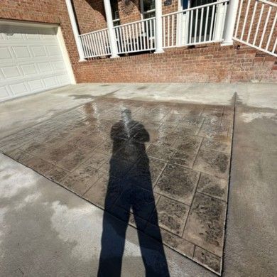 A shadow of a person is cast on a concrete driveway in front of a house.