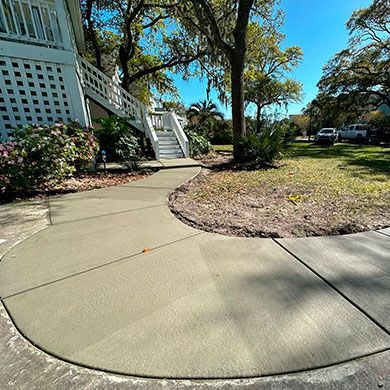 A concrete walkway leading to a house with stairs.