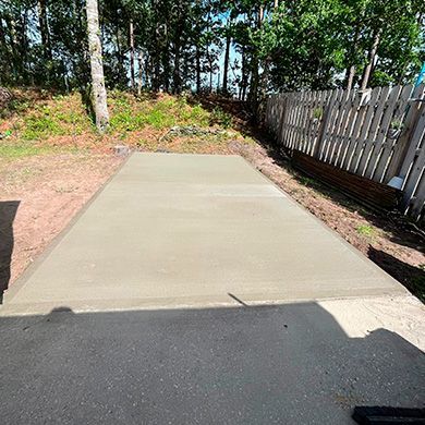 A concrete driveway is being built in a backyard next to a wooden fence.