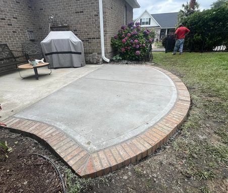 A concrete patio with a brick border is being built in the backyard of a house.