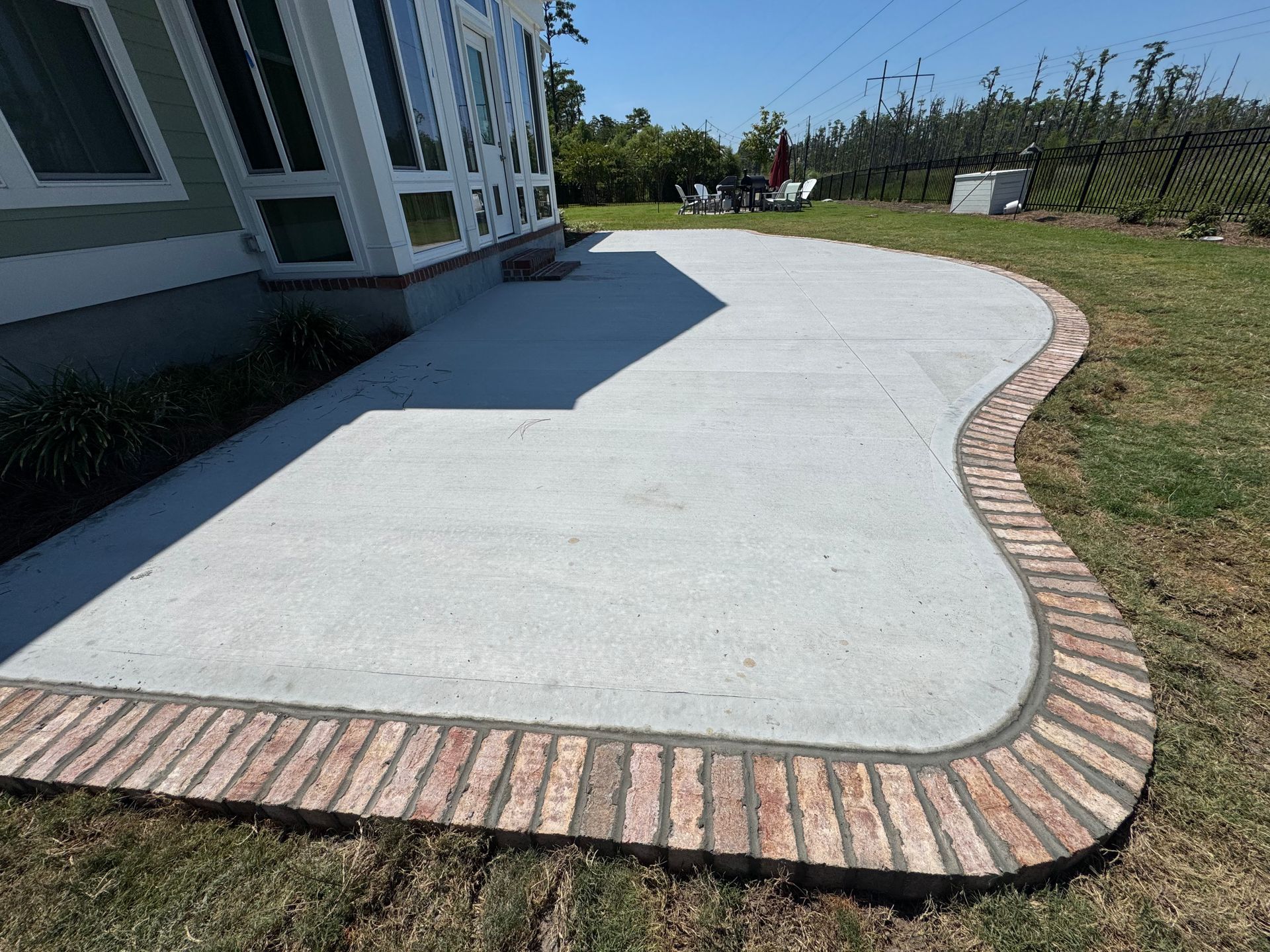 A concrete patio with a brick border is being built in the backyard of a house.