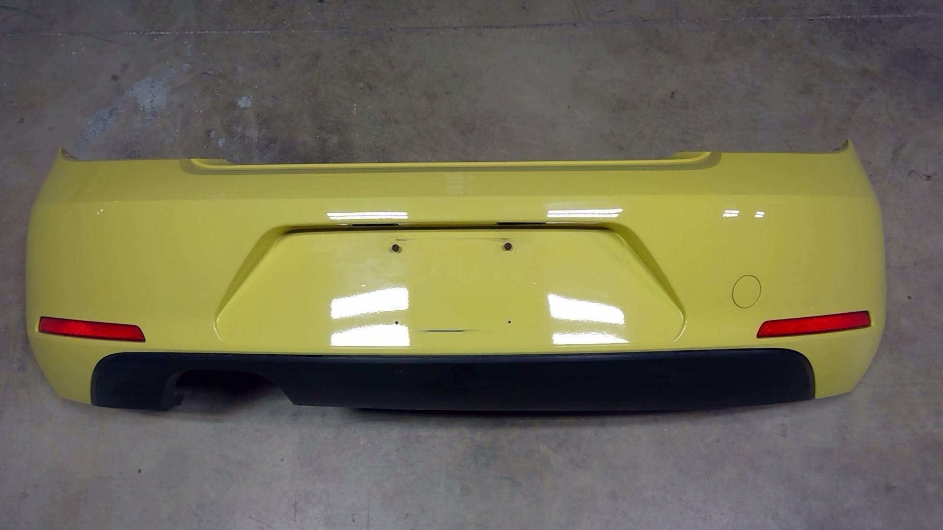 A bright yellow rear bumper for a car, featuring a black lower diffuser, red reflectors, and a license plate indentation.