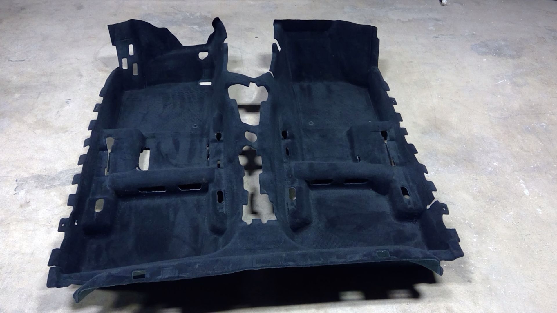 A black molded automotive carpet floor liner with contoured sections for vehicle seats and a center console.