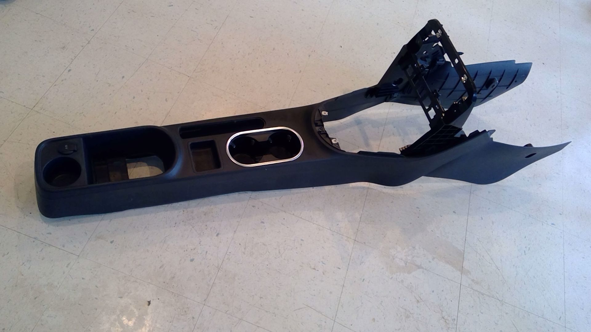 A black plastic car center console interior trim piece resting on a light-colored floor.