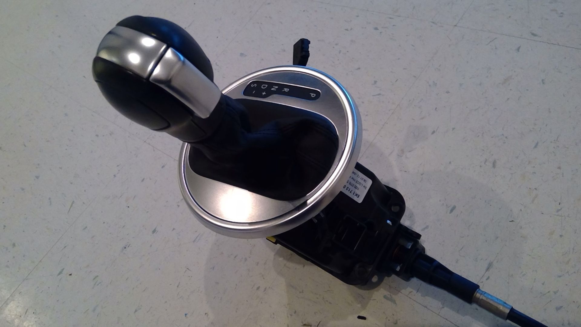 A car's automatic gear shifter assembly featuring a black leather knob with silver trim on a circular metallic base.