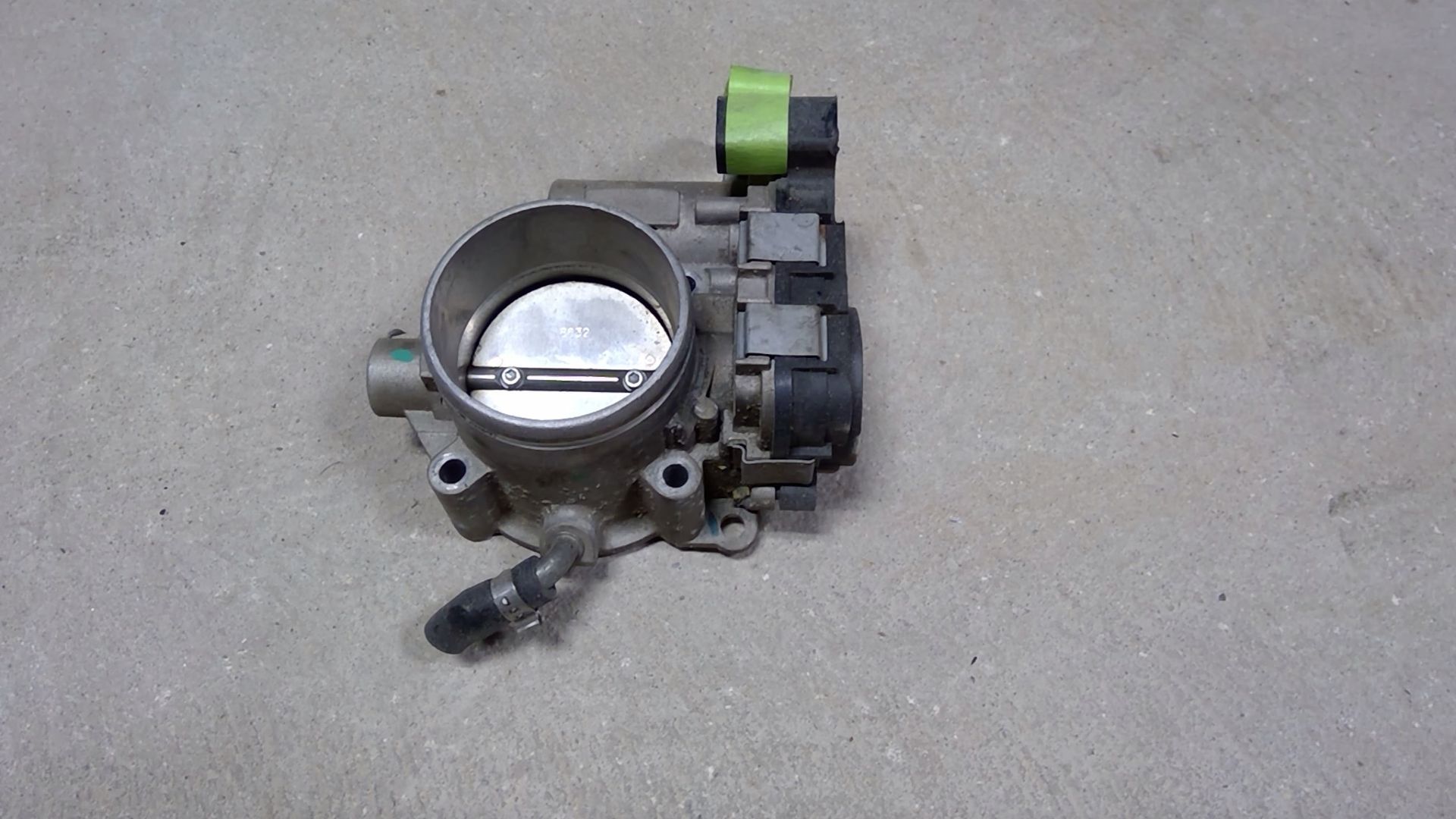 A silver automotive throttle body assembly featuring a green electrical connector and a circular metal valve.
