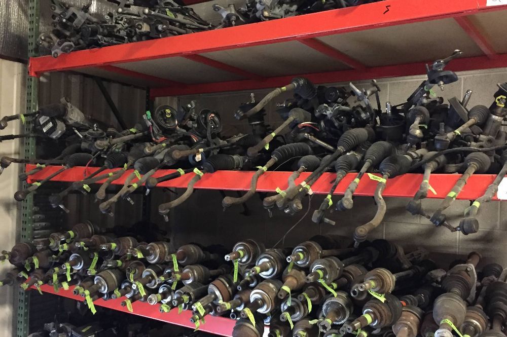 Red warehouse shelves packed with rows of used automotive steering racks and CV axle shafts.