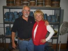 a man and a woman are posing for a picture in front of a shelf filled with barrels .