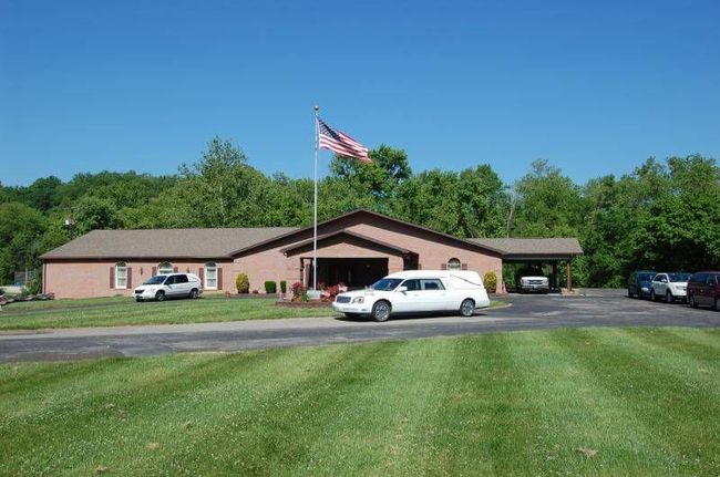 Single-story brick building with an American flag, cars parked in front, and a mowed lawn.