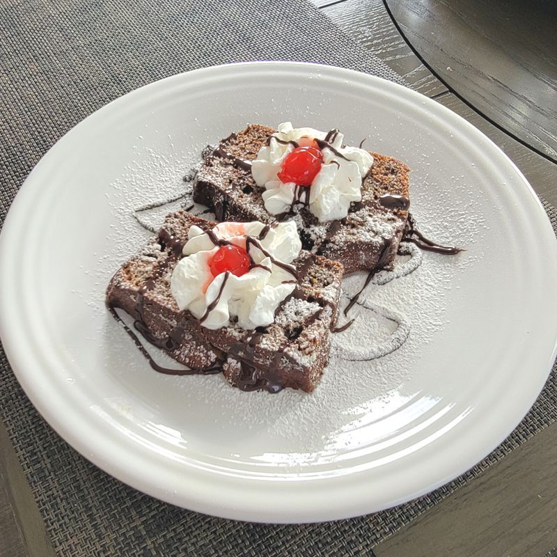 Two brownies with whipped cream and powdered sugar on a white plate