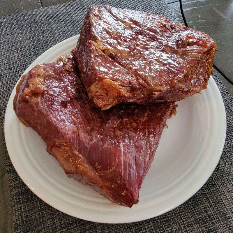 Two pieces of corned beef on a white plate on a table