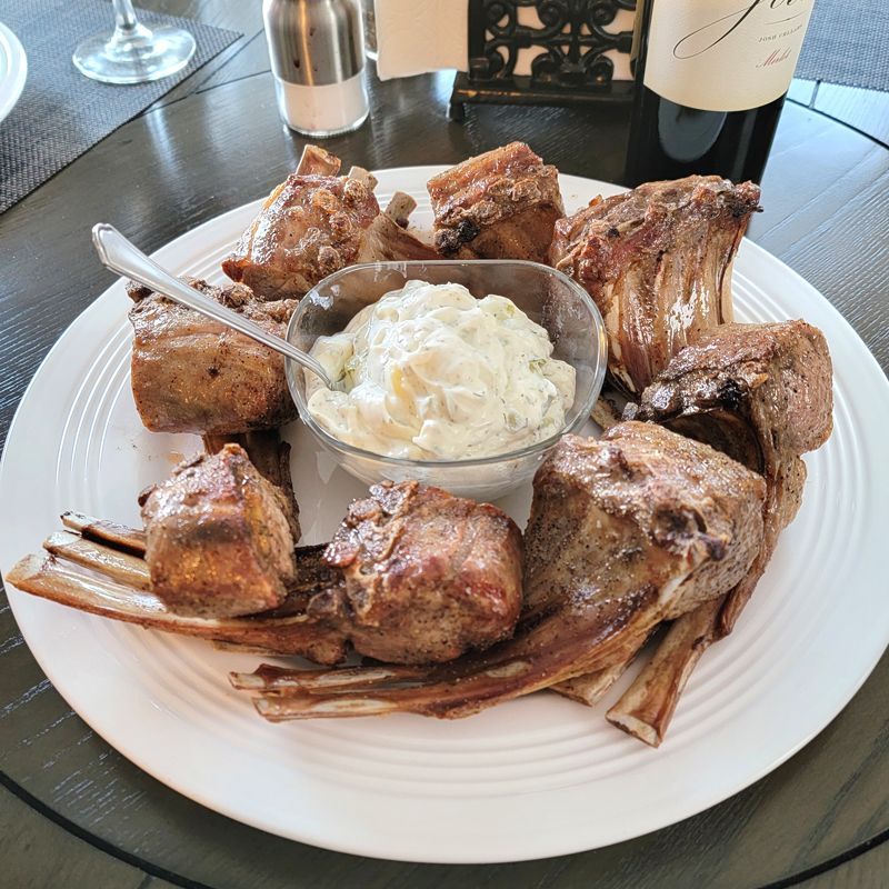 A white plate topped with lamb chops and a bowl of sour cream