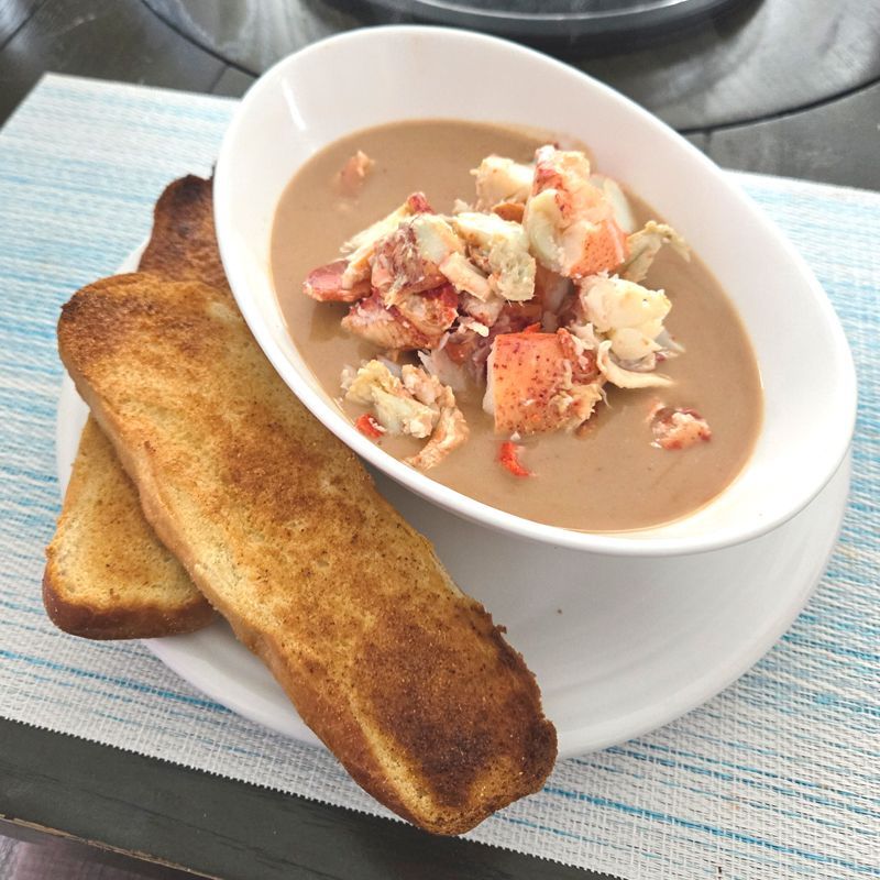 A bowl of lobster bisque with toast next to it