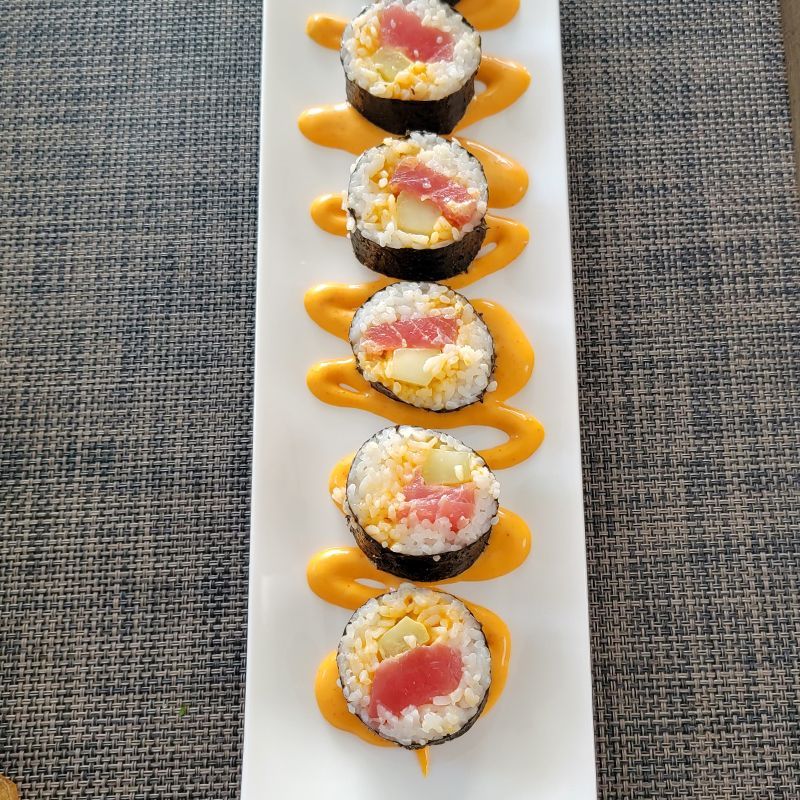 A row of sushi rolls with sauce on a white plate