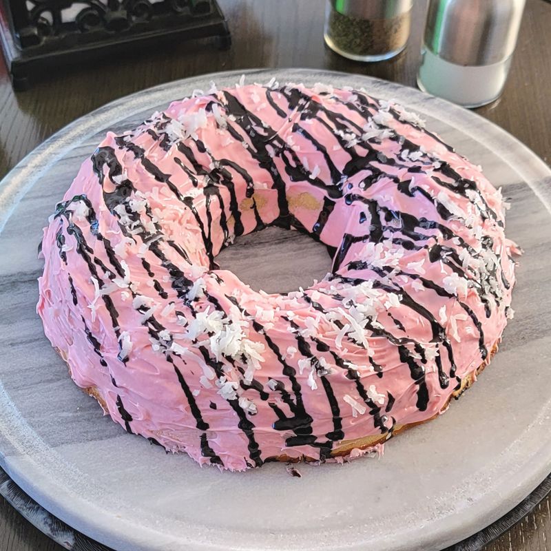 A donut with pink frosting and chocolate sprinkles on a plate