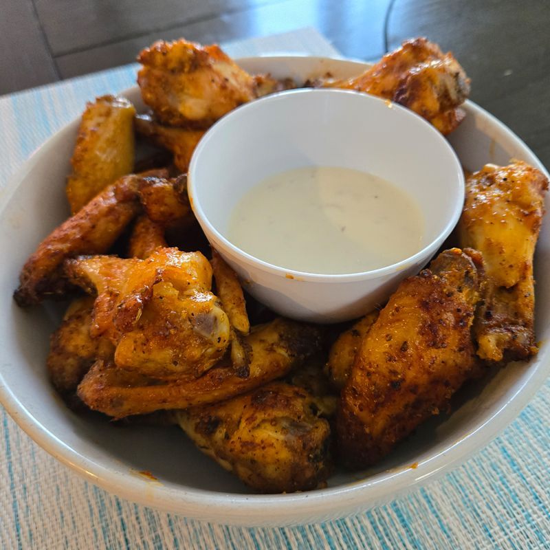 A bowl of chicken wings with a dipping sauce on a table.