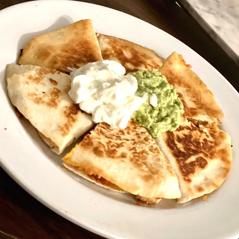 A white plate topped with quesadillas guacamole and sour cream