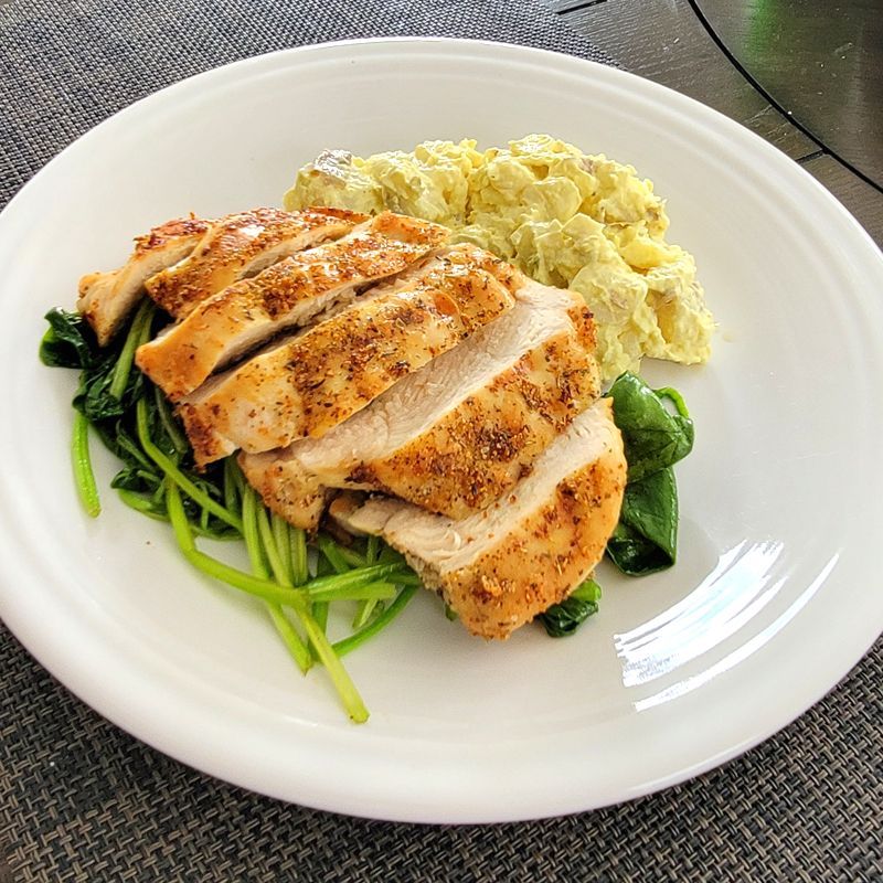 A white plate topped with chicken , spinach and potato salad.