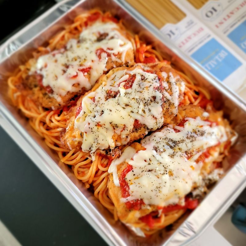 A tray of spaghetti with chicken and cheese on top