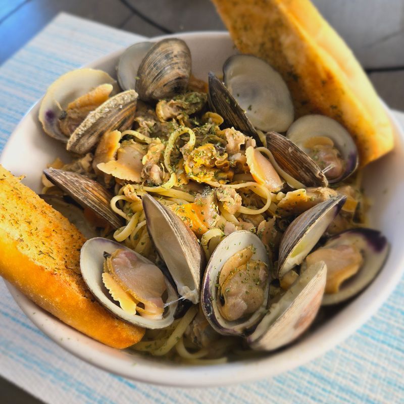 A bowl of clams and noodles with garlic bread