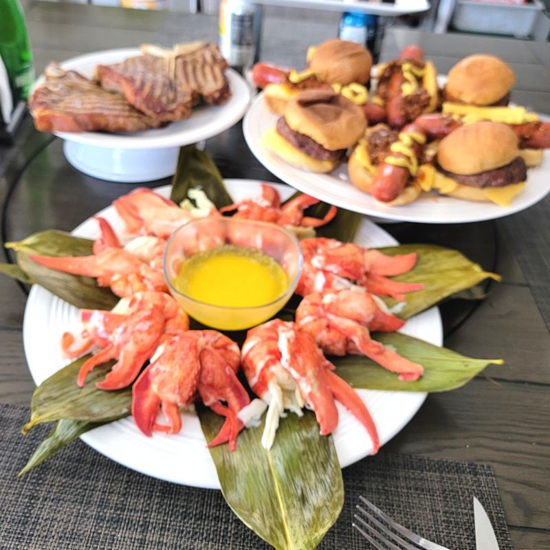 Several plates of food are on a table including lobsters and hamburgers