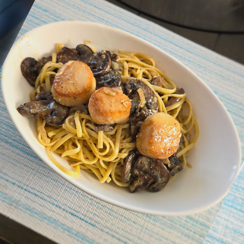 A plate of noodles with scallops and mushrooms on a table