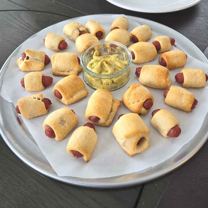 A plate of hot dogs wrapped in dough next to a bowl of mustard