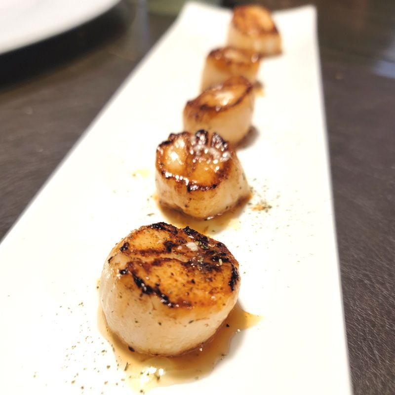 A row of seared scallops on a white plate on a table