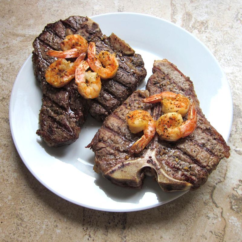 Two porterhouse steaks and shrimp on a white plate