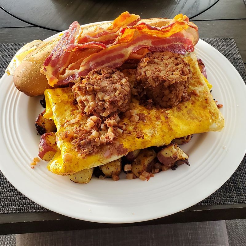 A plate of food with eggs , bacon , sausage and potatoes on a table.