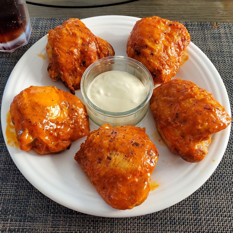 A white plate topped with buffalo chicken thighs and a bowl of ranch dressing