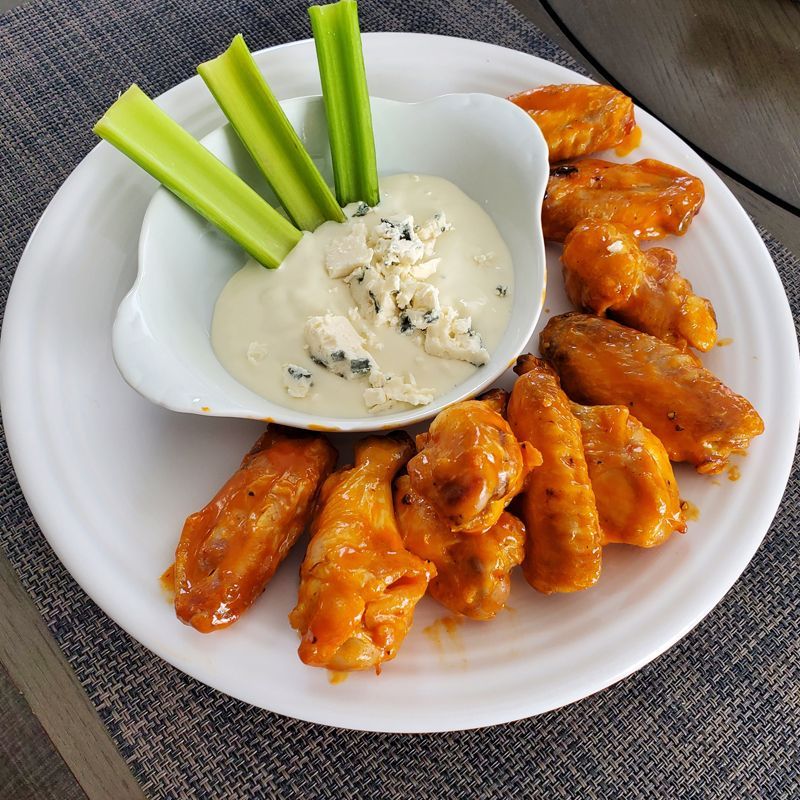 A white plate topped with chicken wings and a bowl of blue cheese dressing