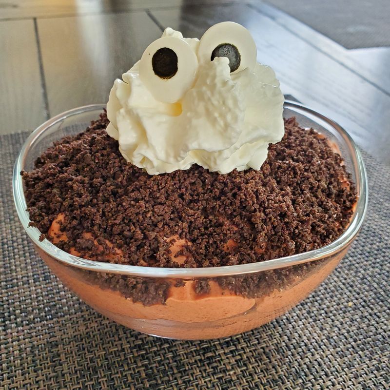 A bowl of pudding with whipped cream and chocolate crumbs on top