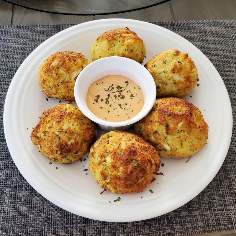 A white plate topped with crab cakes and a small bowl of dipping sauce