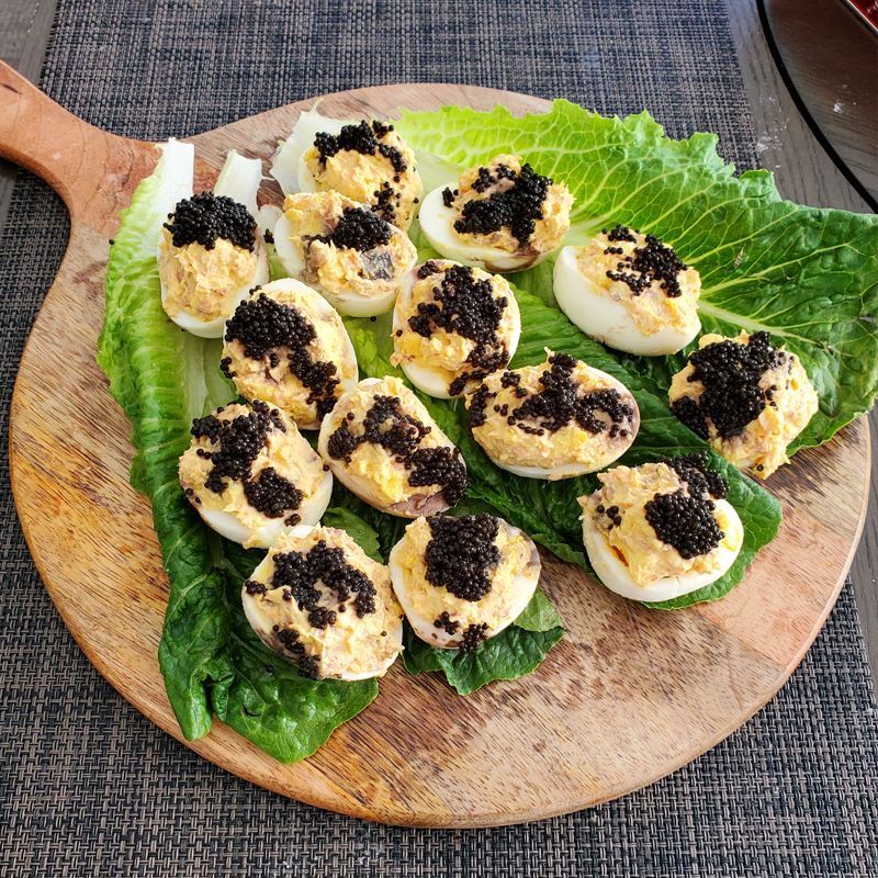 A wooden cutting board topped with stuffed eggs and imported Beluga Sturgeon caviar.