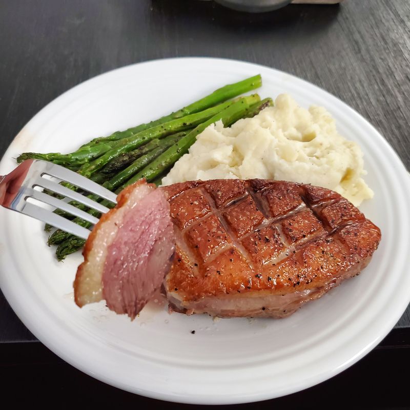 A white plate topped with wild duck breast mashed potatoes and asparagus