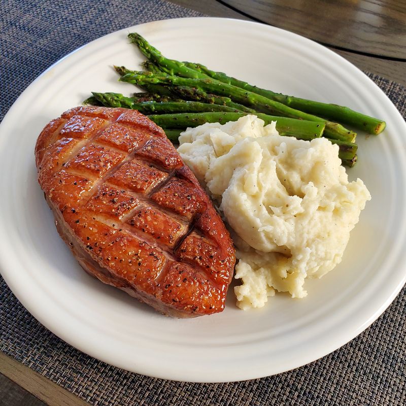 A white plate topped with duck breast mashed potatoes and asparagus