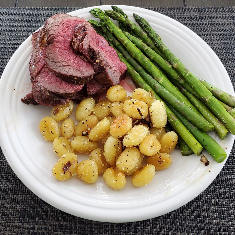 A white plate topped with meat asparagus and gnocchi