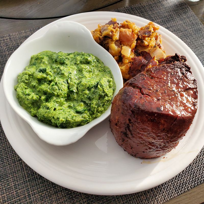 A white plate topped with a steak and a bowl of green mashed potatoes