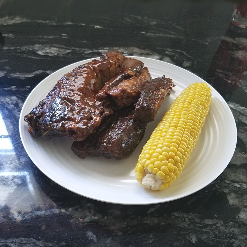 Ribs and corn on the cob on a white plate