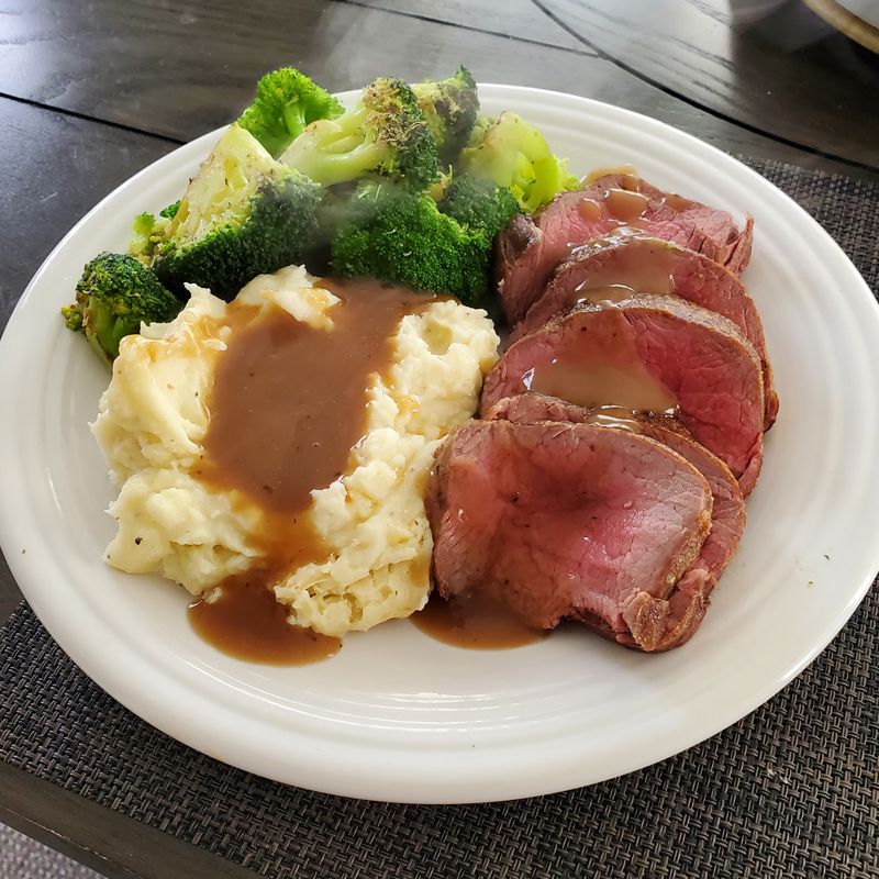 A white plate topped with steak , mashed potatoes , broccoli and gravy.