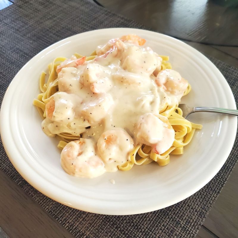 A white plate topped with shrimp alfredo over linguine with a fork on a table.