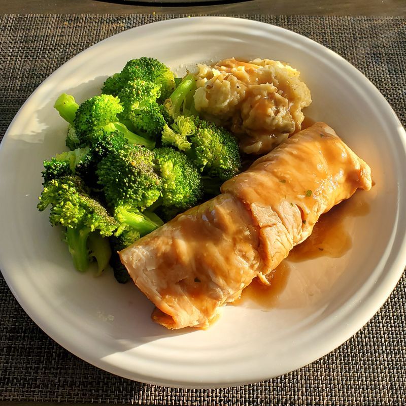 A plate of food with stuffed turkey broccoli and mashed potatoes on a table.