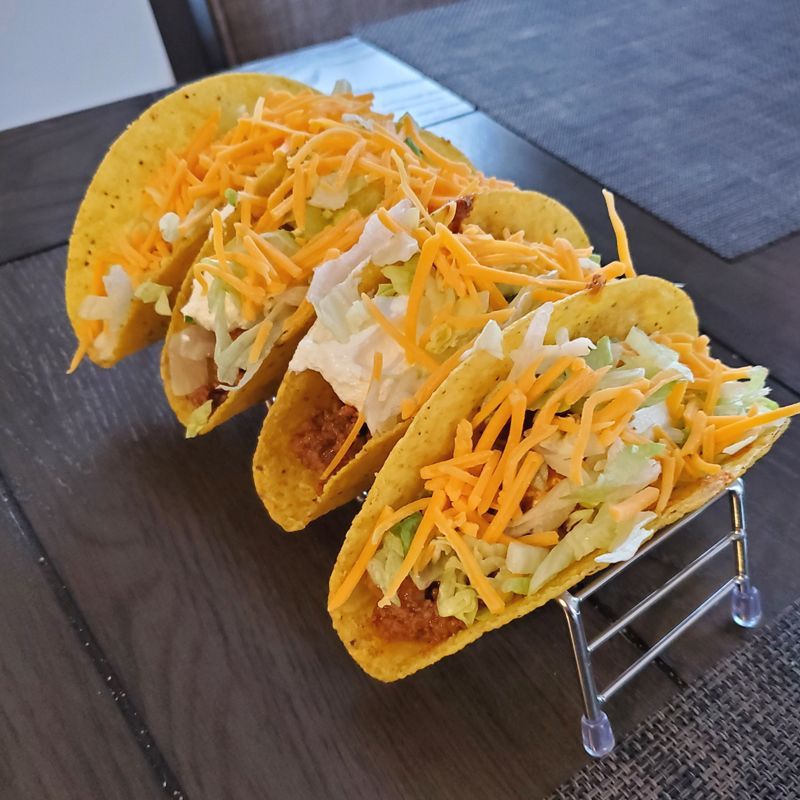 Three tacos are sitting on a metal stand on a wooden table.