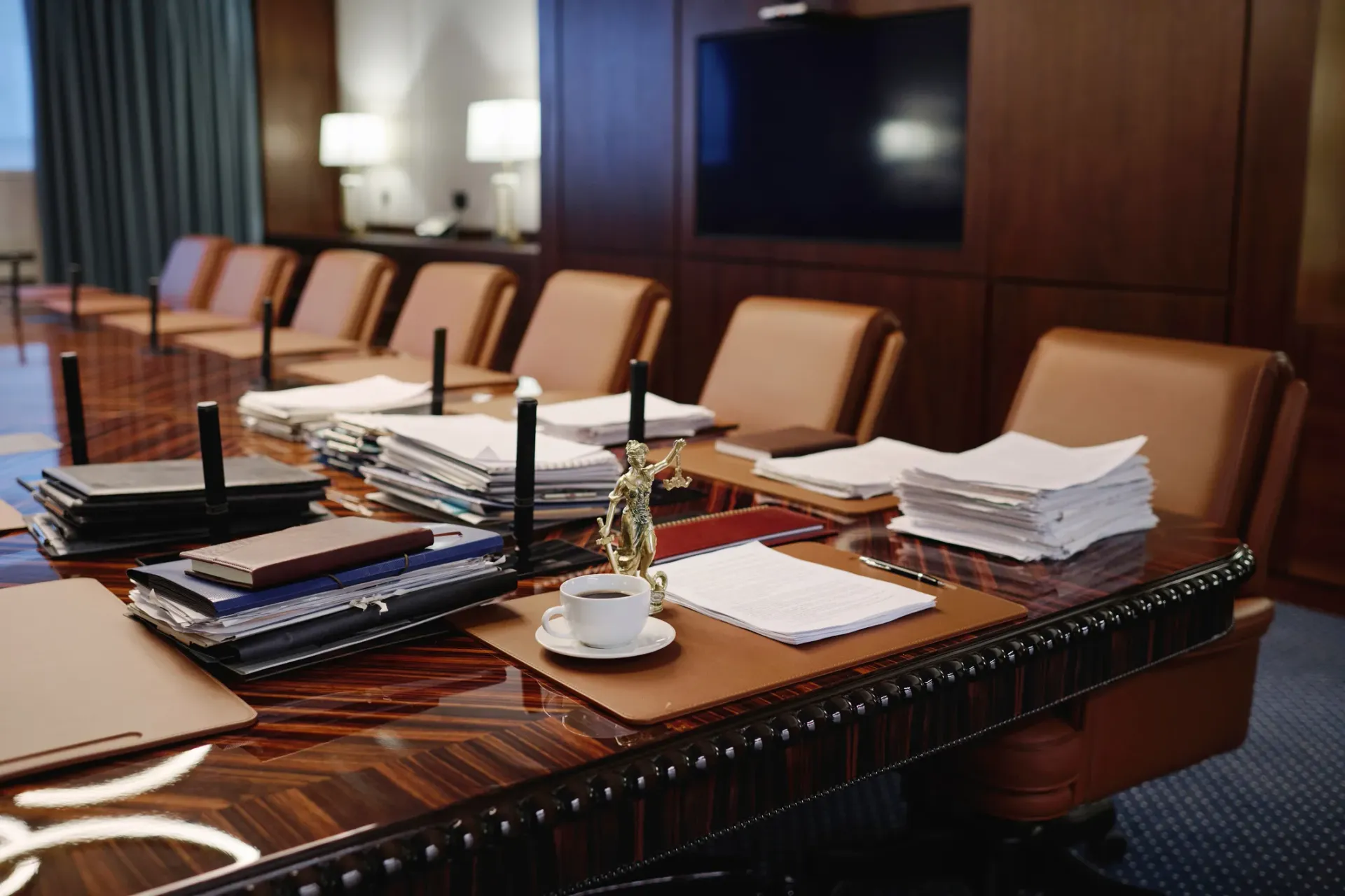 Conference room with a large, wood desk covered in papers and notebooks. Leather chairs are behind the desk.