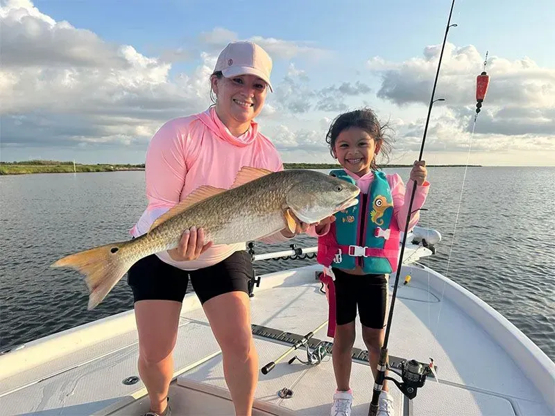 A woman and a little girl are standing on a boat holding a large fish.